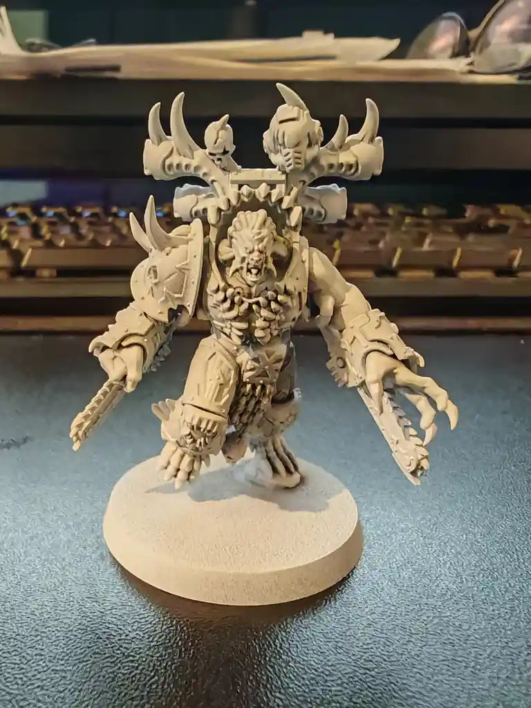 A heavily detailed, unpainted fantasy miniature of a monstrous, horned warrior with skeletal armor and multiple skulls on…
