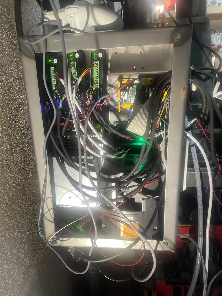 A messy, tangled mess of wires and electronic components inside a metal enclosure, with a white video game controller…