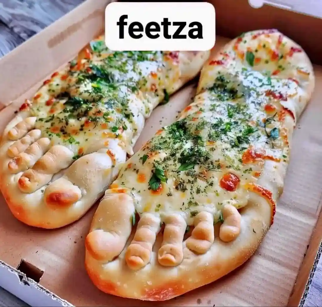 Two pizza slices shaped like human feet, complete with toes, are presented in a cardboard pizza box. They are topped with…