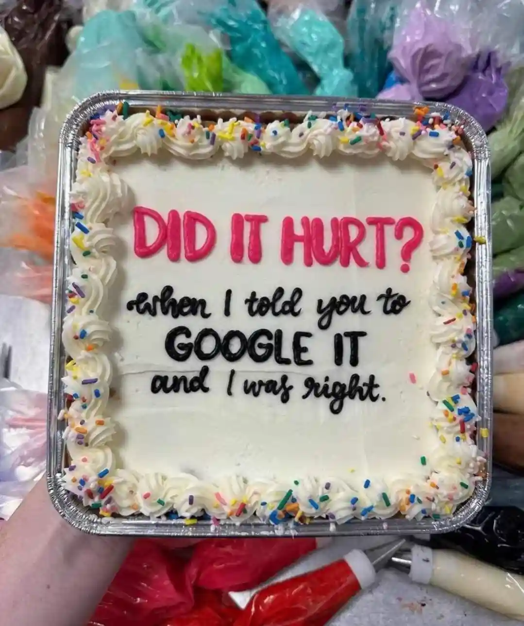 A square cake with white frosting and colorful sprinkles is held in a foil pan, featuring the text 'DID IT HURT? when I told…
