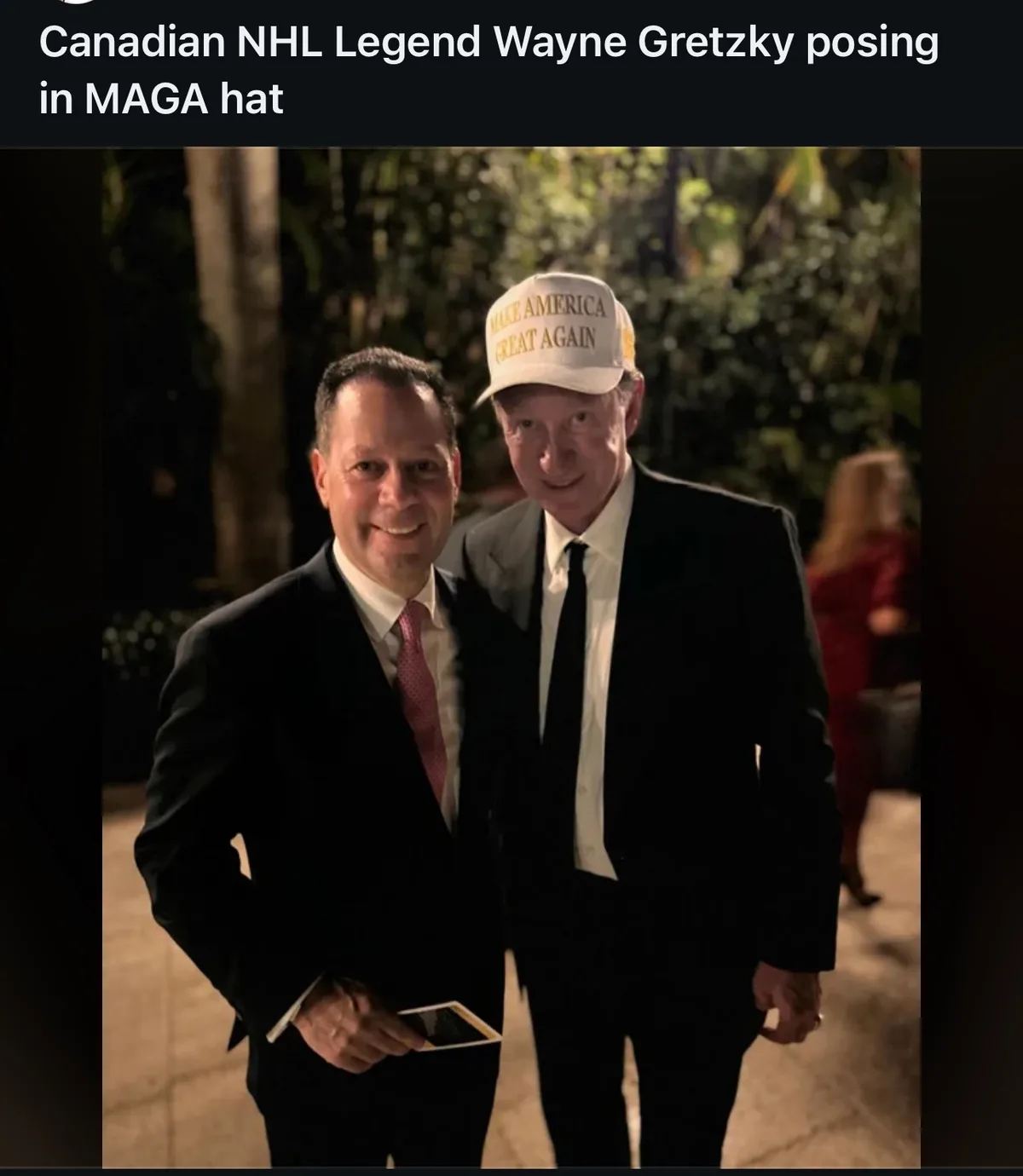 Two men in suits pose for a photo at night outdoors; the man on the right, identified as Wayne Gretzky, wears a white 'MAKE…