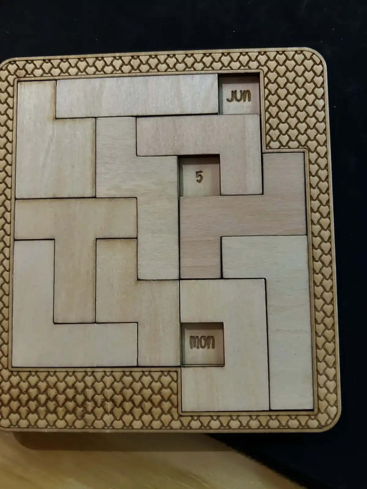 A wooden puzzle calendar with interlocking pieces forming a grid, showing 'jun' (June), the number '5', and 'mon' (Monday)…