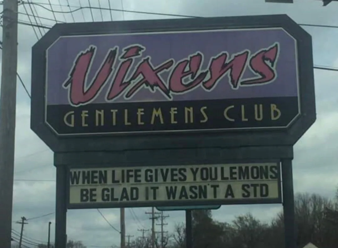 A sign for 'Vixens Gentlemens Club' features a humorous, altered version of the 'when life gives you lemons' adage, reading…