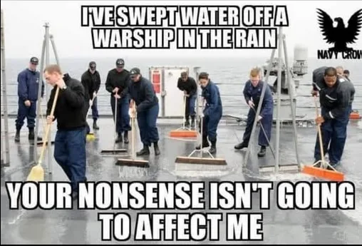 A group of sailors in navy uniforms are sweeping water off the deck of a warship while it is raining. The image has large…