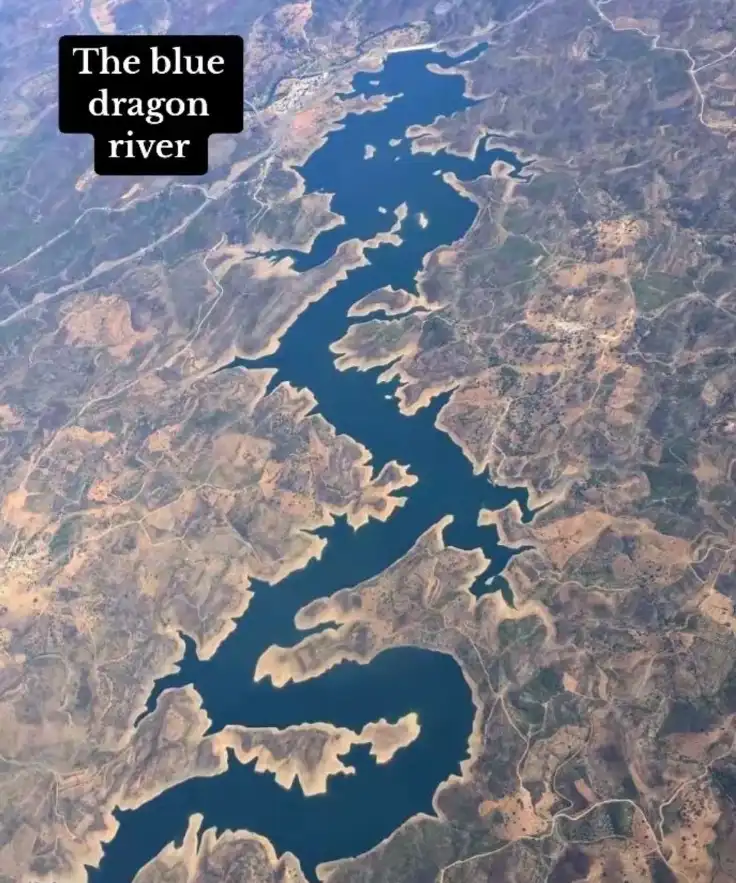 An aerial satellite image shows a winding, deep blue waterway snaking through arid, brownish terrain with visible landforms…