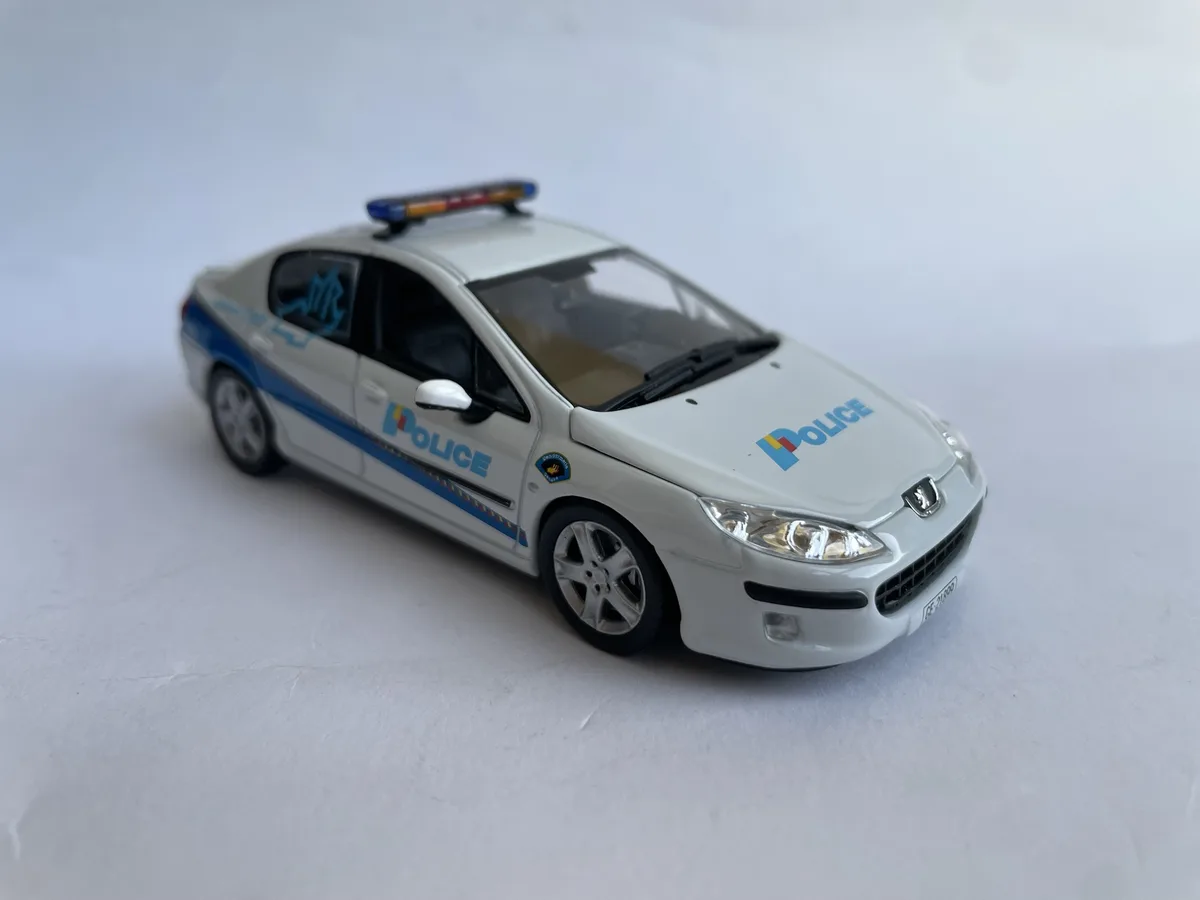 A white toy police car with blue stripes and 'POLICE' lettering on the hood and side, featuring a roof-mounted light bar, is…