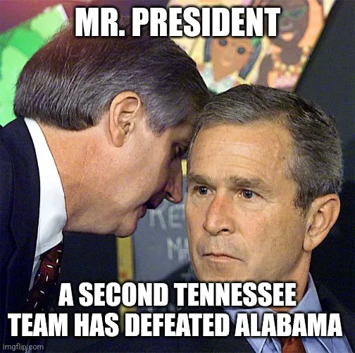 A man in a suit leans in close to former president George W. Bush, who looks unimpressed. White text overlays the image…