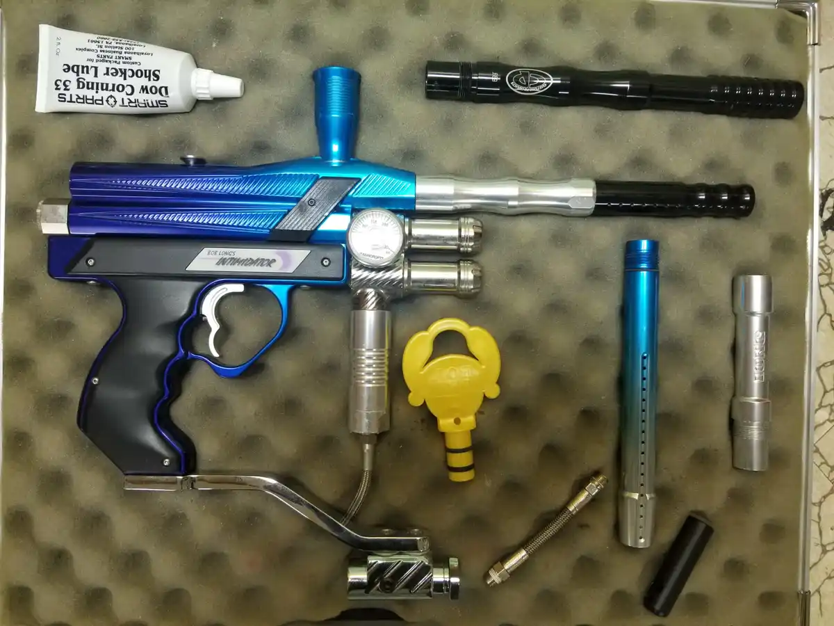 An overhead shot displays a blue and black paintball marker, labeled 'BOB LONG'S INTIMIDATOR', laid out with its various…