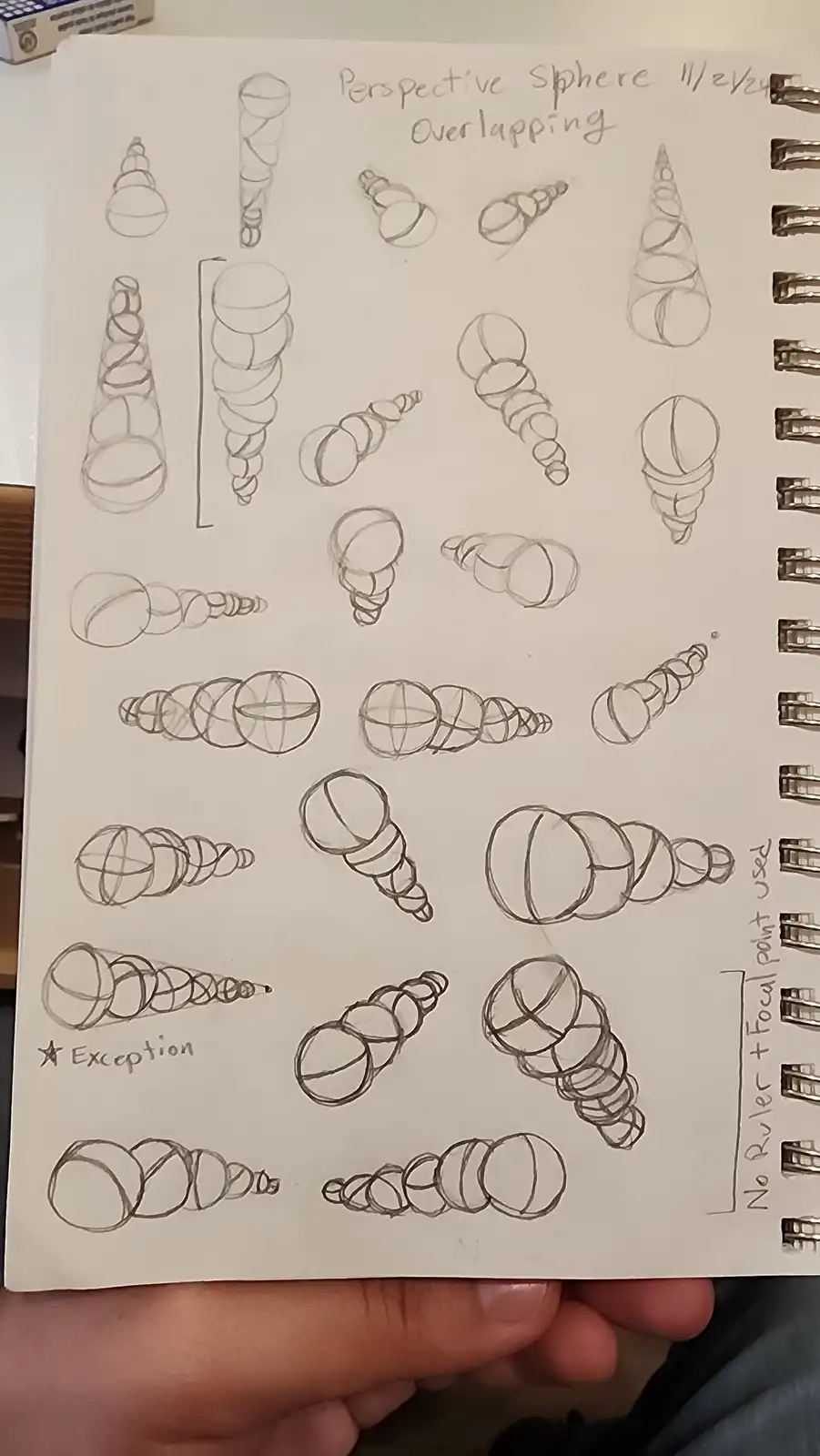 A hand holds a sketchbook page filled with numerous pencil drawings of spheres in various overlapping and perspective…