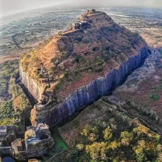 an aerial view of a steep, rocky hill with ancient stone ruins perched on its summit and along its cliffs, overlooking a…