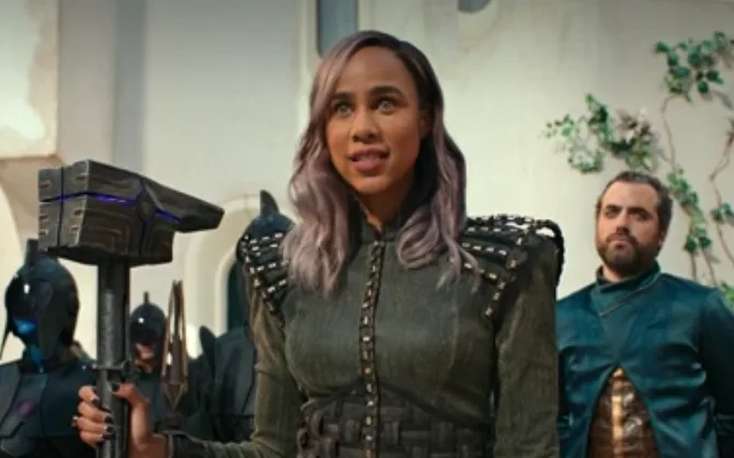 A woman with purple-tipped hair, wearing a studded green outfit, holds a large futuristic hammer with glowing blue accents…