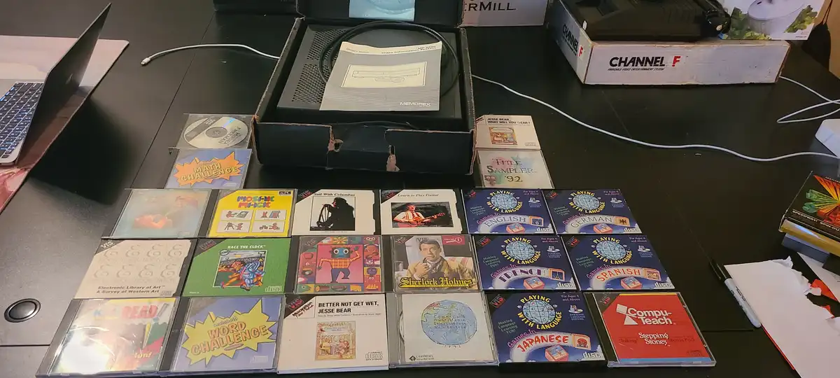 A collection of vintage educational software discs for a video game console, arranged on a desk next to the console's box…