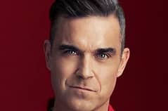 A close-up portrait of a man with dark hair and intense eyes, wearing a red shirt against a solid red background. The image…
