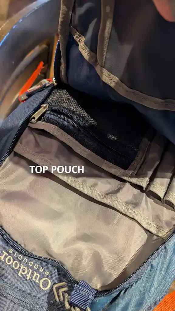 A close-up photo shows the inside of an empty blue and gray backpack, with the text 'TOP POUCH' overlaid in white. The…