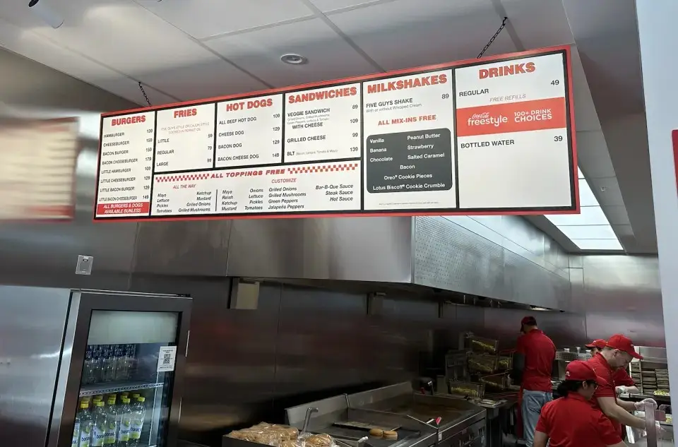 A photo of a Five Guys restaurant menu board showing various food categories like burgers, fries, hot dogs, sandwiches…