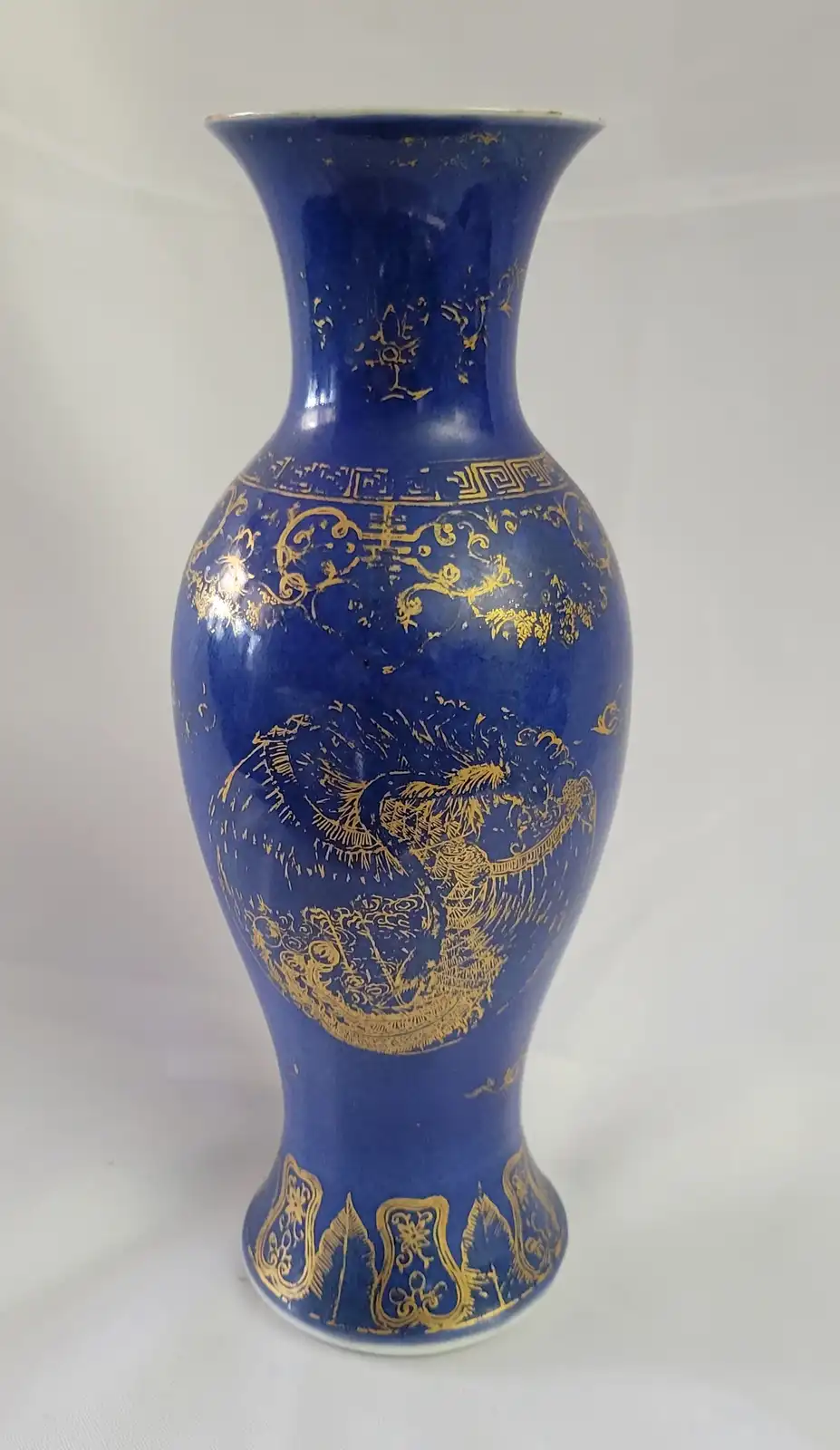 a tall, blue ceramic vase with gold decorative patterns, including a prominent dragon design, shows visible wear and…