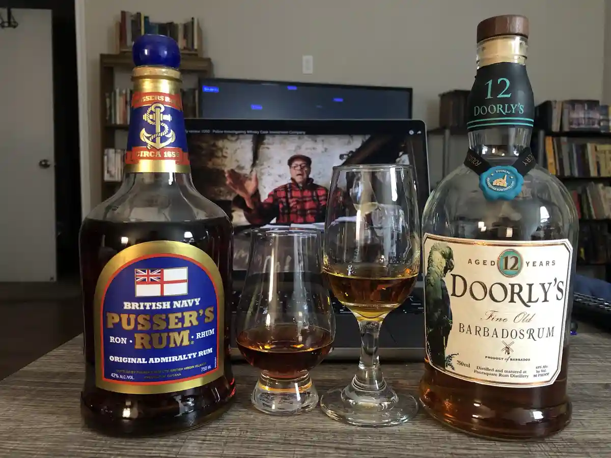 Two rum bottles, Pusser's British Navy Rum and Doorly's 12-Year-Old Barbados Rum, flank two tasting glasses on a wooden…