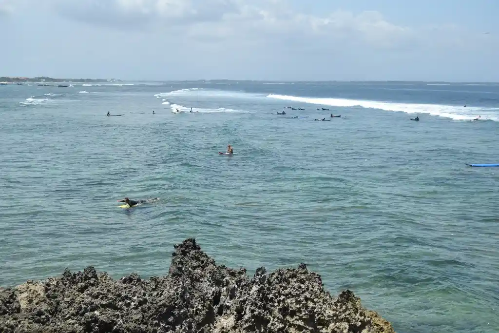A wide-angle photo of a crowded surf break with numerous surfers on boards in the ocean, some paddling, others waiting for…
