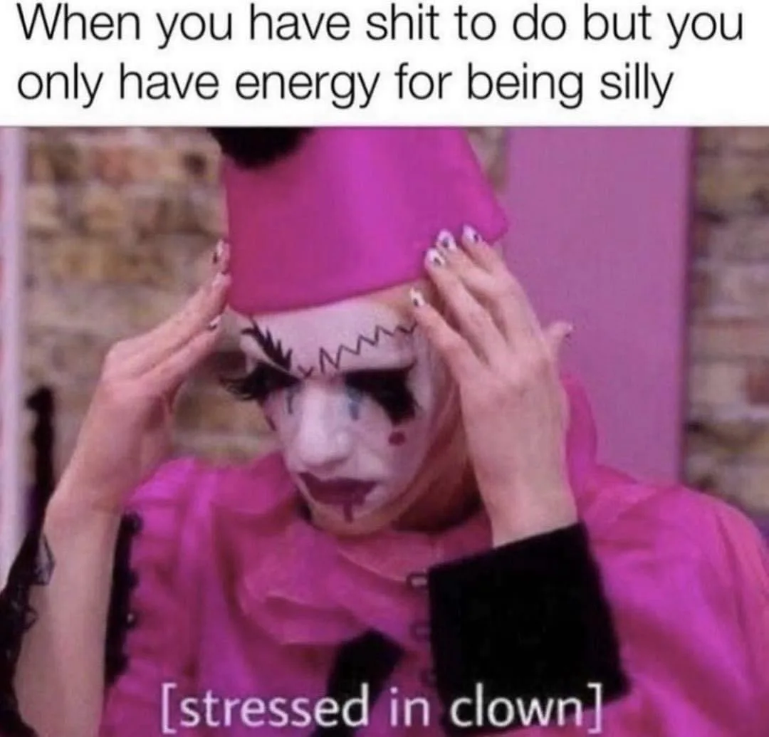 A person dressed as a clown in a bright pink outfit and hat, with white face paint, black zigzag eyebrows, and red lips…