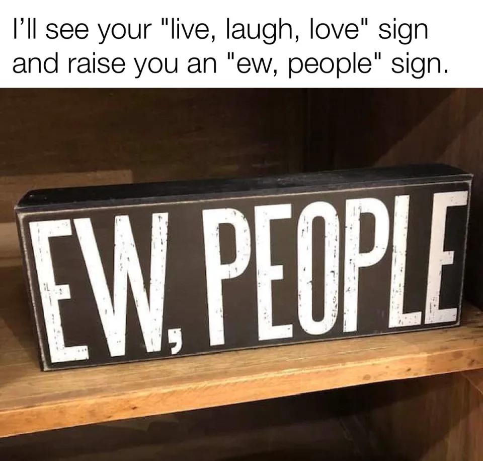A black rectangular wooden sign with white distressed lettering reading "EW, PEOPLE" sits on a light brown wooden shelf…