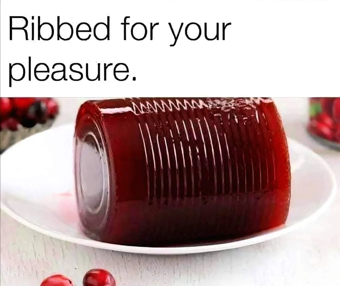 A glossy, deep red jelly dessert shaped like a can, sitting on a white plate, with visible ribbed texture mimicking a can's…