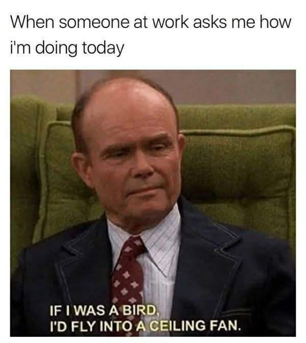 A still image of a man with a balding head and a weary expression, wearing a suit and tie, seated in a green armchair. The…