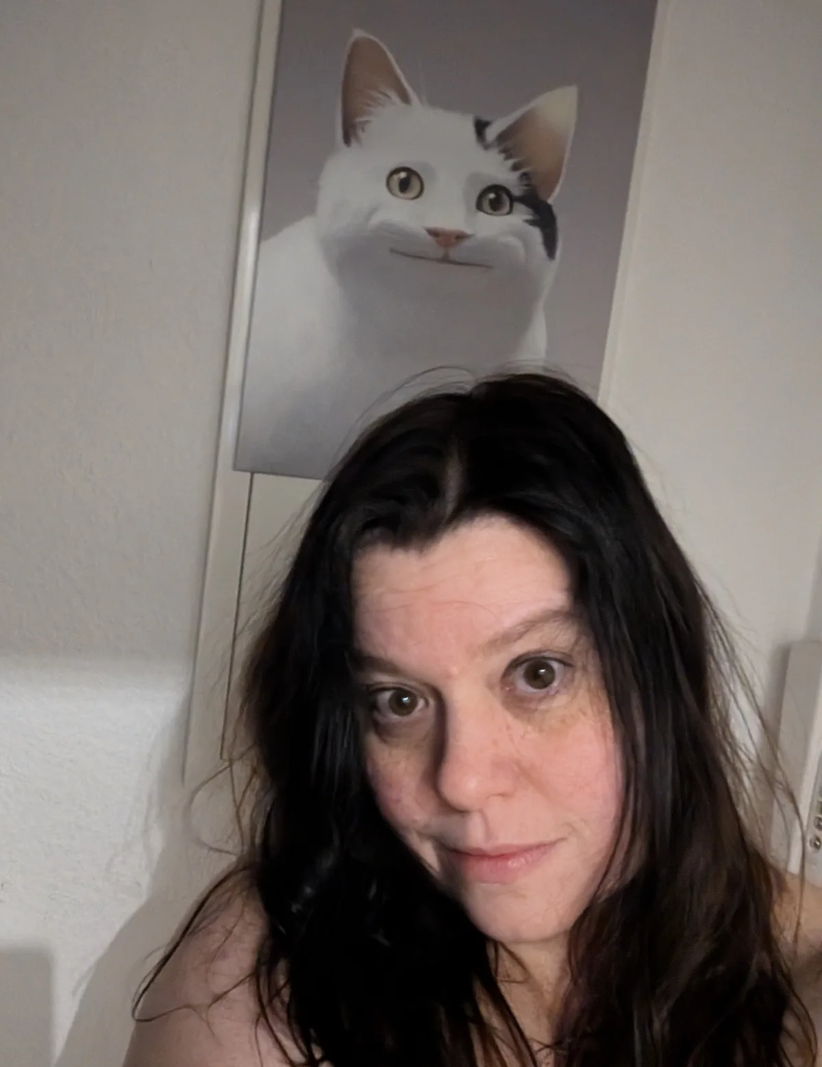 A person with dark hair and freckles looks at the camera with a slightly confused or weary expression. Behind them, mounted…