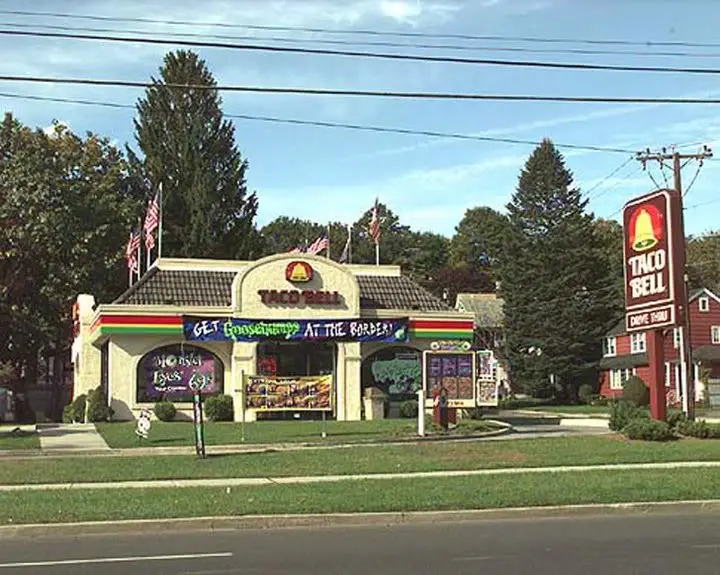 A Taco Bell restaurant with a large sign that reads 'GET Goosebumps AT THE BORDER!' in blue letters. The building has the…