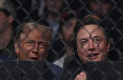 Two men, identified as Donald Trump and Elon Musk, are shown behind a chain-link fence, looking toward the right with…