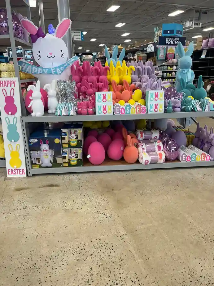 A brightly lit retail store aisle displays a massive, colorful assortment of Easter decorations including inflatable…