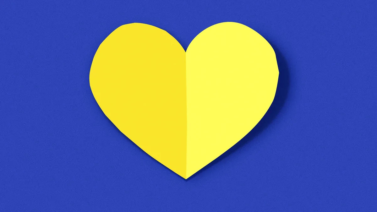 A yellow paper heart cut in half and folded along its vertical axis, creating a 3D effect against a solid blue background…