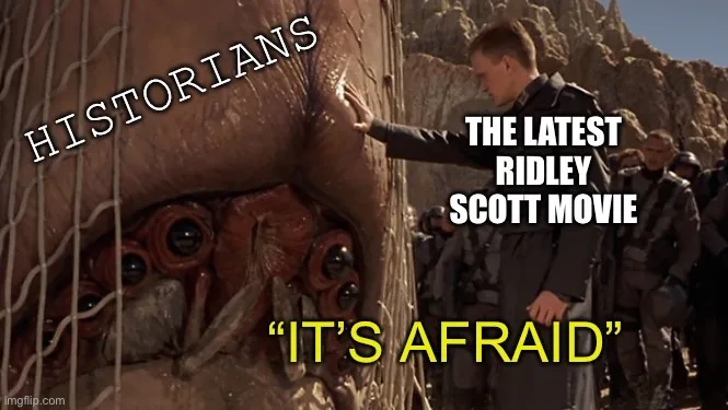 A man in a dark uniform reaches out to touch the skin of a large, multi-eyed alien creature encased in a netted structure…
