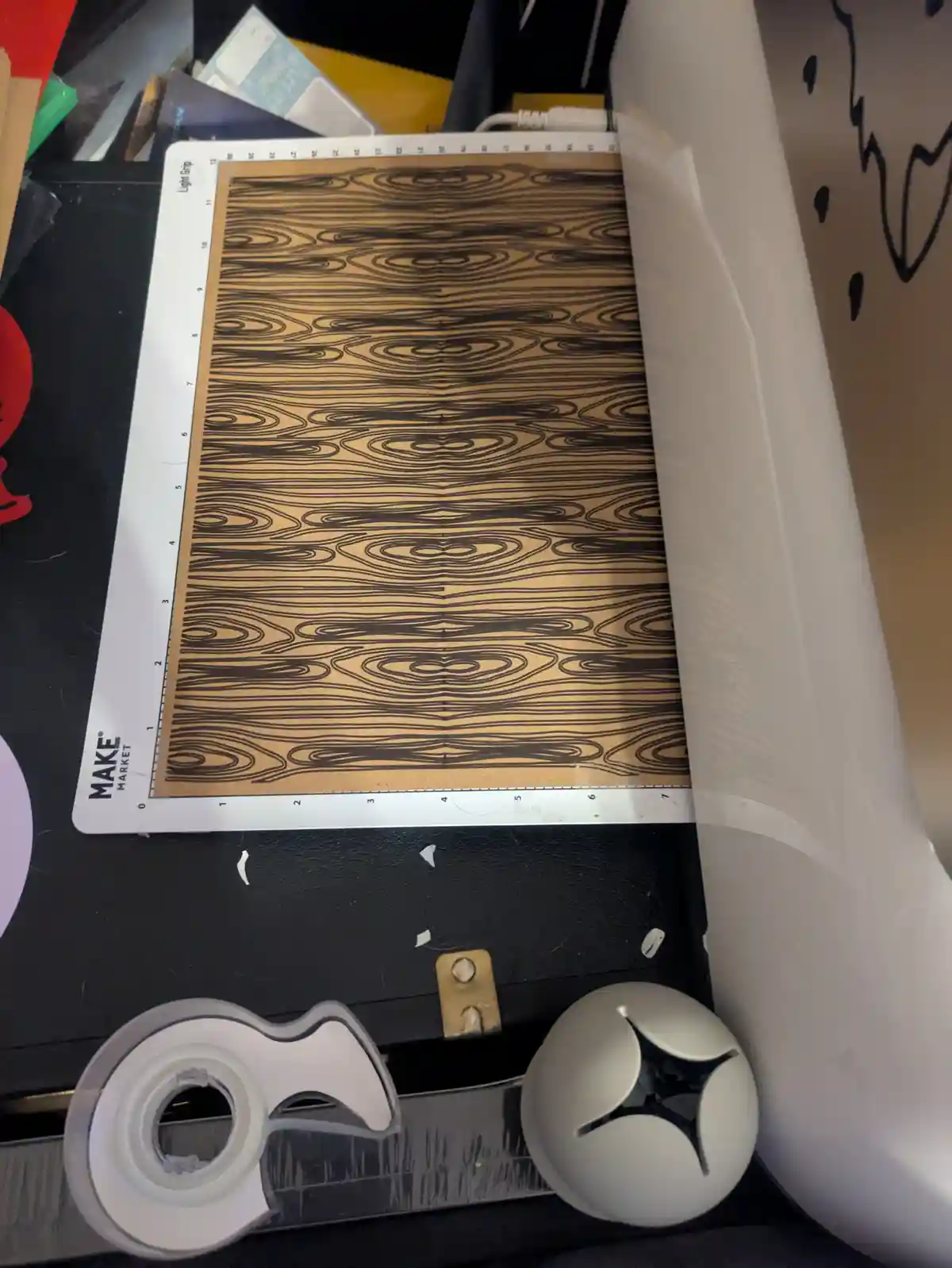 A close-up photo shows a white 'MAKE MARKET' cutting mat with a brown paper sheet featuring a symmetrical, swirling wood…