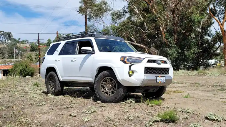 A white Toyota 4Runner with aftermarket modifications, including a roof rack labeled 'GOBI', large off-road tires, and a…
