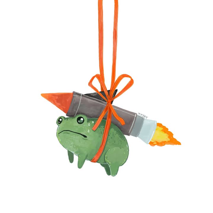 A green cartoon frog with a sad, teary-eyed expression is strapped to a rocket with an orange ribbon bow. The rocket is…