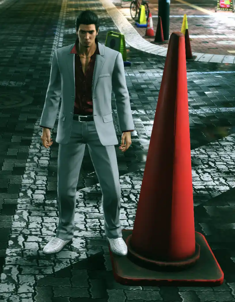 A man in a grey suit and red shirt stands on a wet cobblestone street next to a large red traffic cone. The cone is…