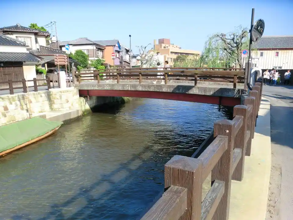 A photo of a wooden pedestrian bridge over a canal in a Japanese town, with people walking across and others standing on the…