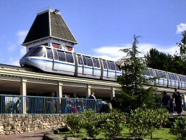 A silver and blue monorail train is visibly tilted at an extreme angle, appearing to be precariously balanced or falling off…