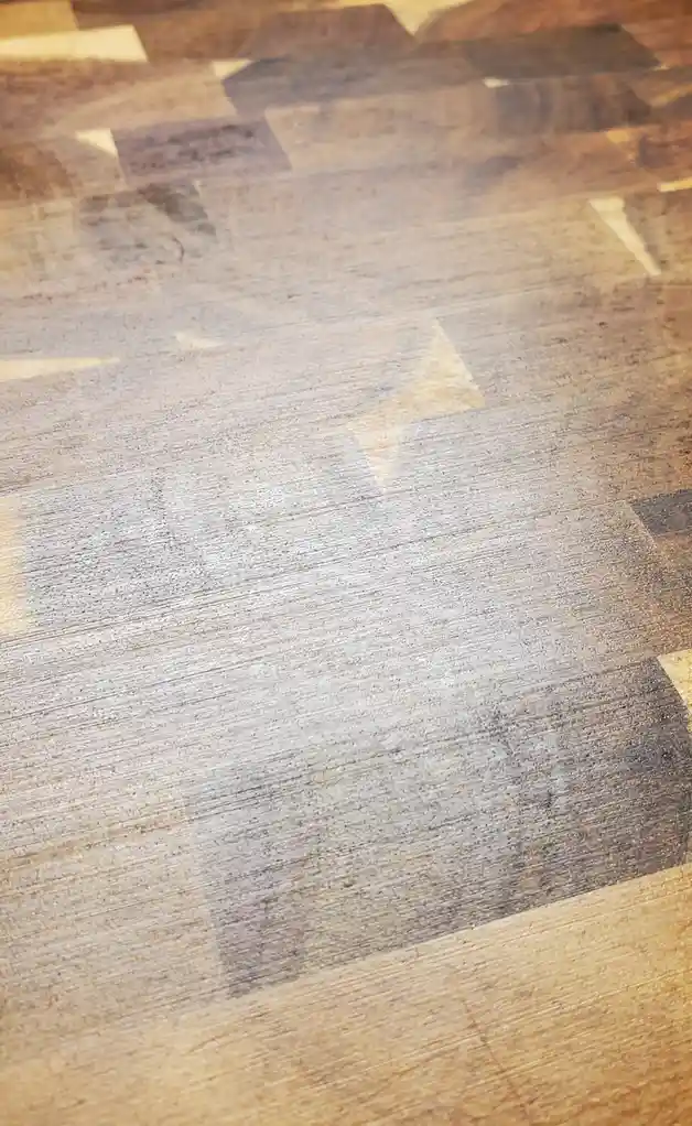 A close-up of a heavily used wooden cutting board with visible scratches, stains, and worn areas, overlaid with the text…