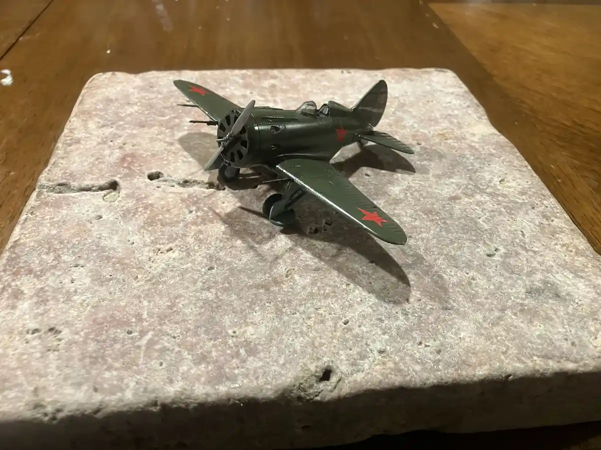 A small green model airplane with red star insignias on its wings and fuselage sits on a rough, pitted stone slab. The stone…