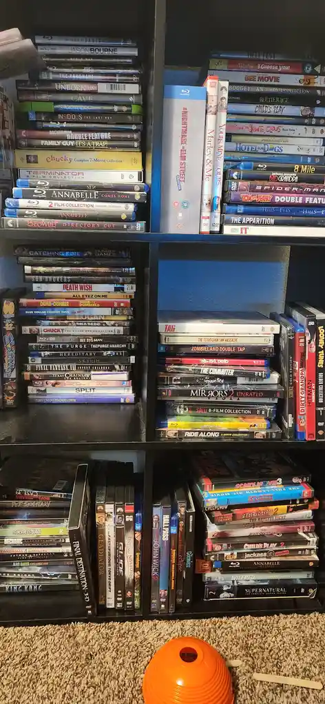 A photo of a densely packed black media shelf filled with hundreds of DVDs and Blu-rays of various genres, including horror…