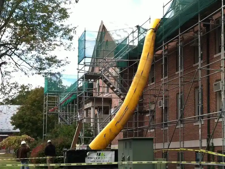 A construction site features a large, bright yellow flexible tube, resembling a giant banana, attached to the side of a…