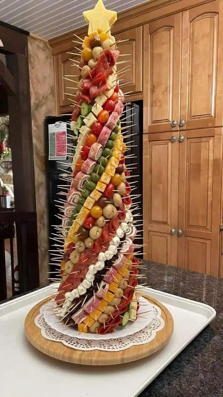 A tall, cone-shaped food arrangement resembling a Christmas tree, constructed from skewers holding various meats, cheeses…