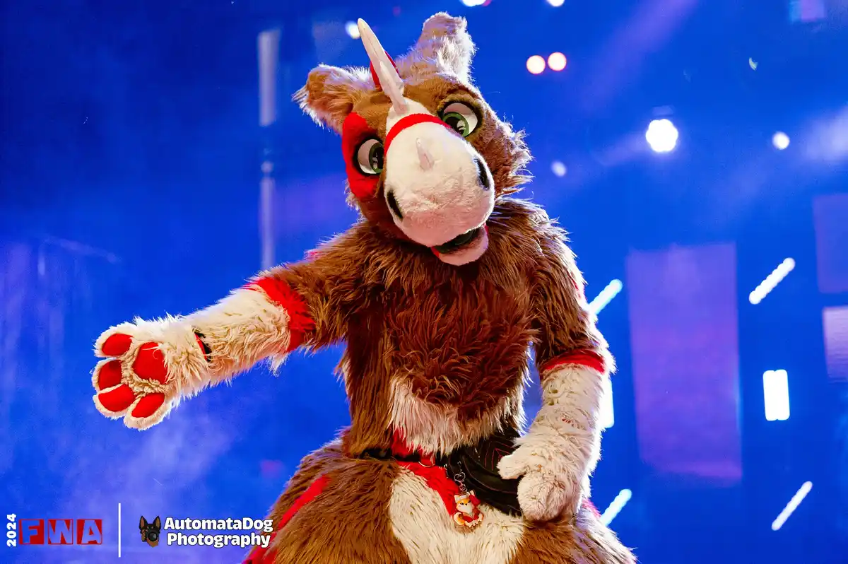 A person in a detailed brown and white furry costume resembling a rhino with a single horn, red accents, and large green…