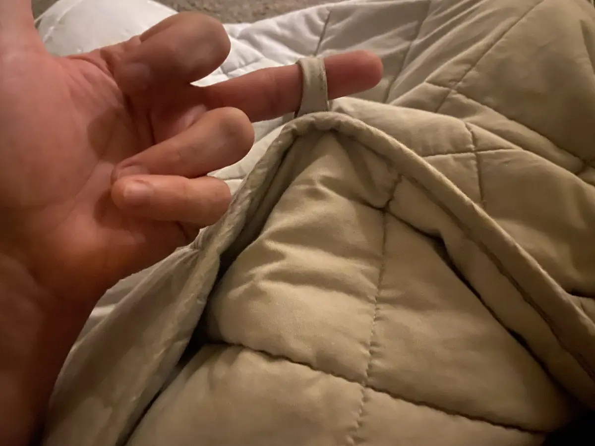 A close-up photo shows a person's hand with their index finger looped through a small fabric loop on the edge of a beige…