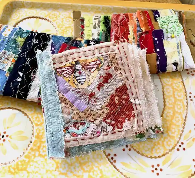 A colorful, handmade patchwork quilt made from scraps of various fabrics, including a prominent embroidered bee, is…