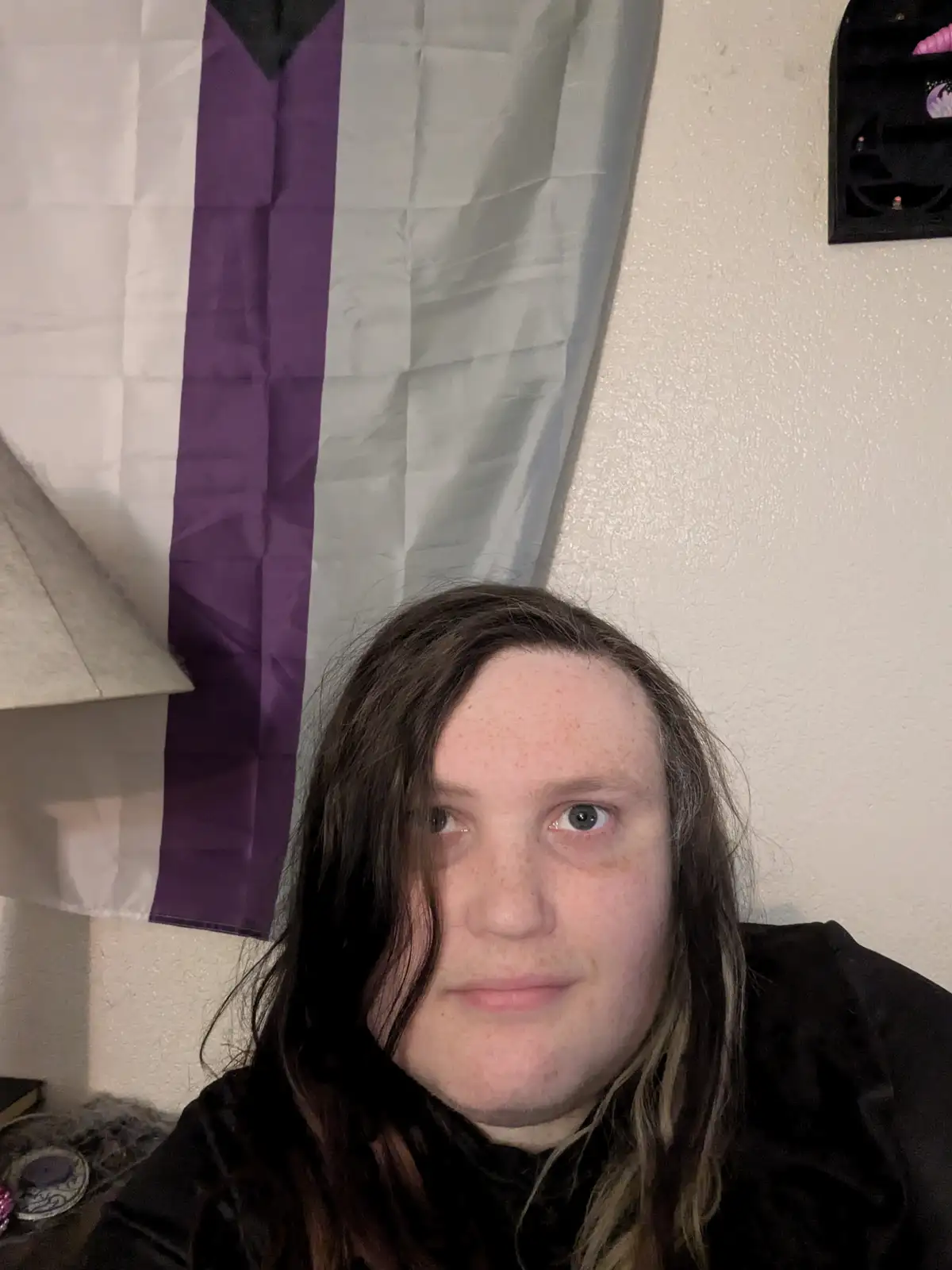 A person with long brown hair and freckles stares directly at the camera with a tired, unimpressed expression. Behind them…