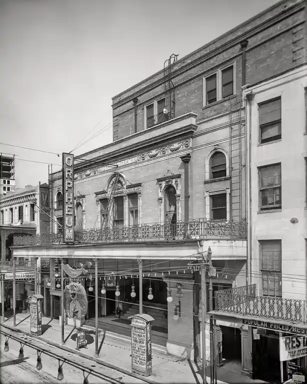 A black-and-white historical photograph of the Orpheum Theatre, showing its ornate brick facade, marquee, and surrounding…