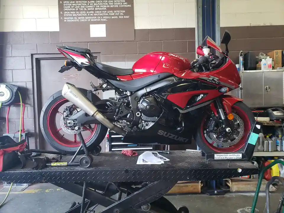 A red and black Suzuki GSX-R motorcycle is elevated on a hydraulic lift in a garage, with a sign on the wall behind it…