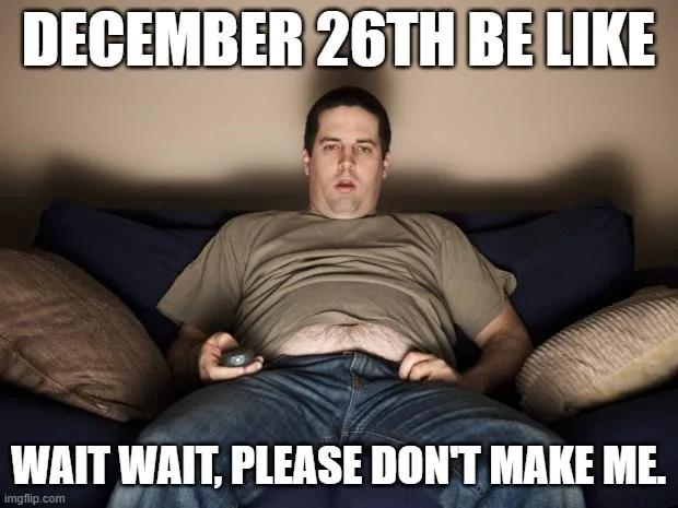 A man with a surprised, pleading expression sits on a couch holding a remote, wearing a brown t-shirt and jeans. The text…